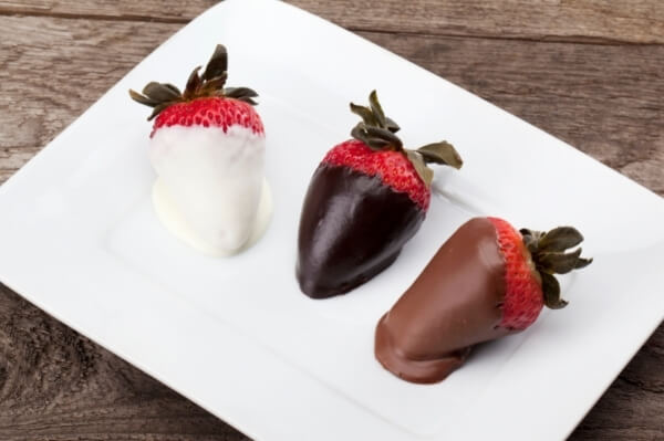Tres fresas  bañadas en chocolate, cada una de un color, a la izquierda chocolate blanco, en el medio chocolate negro, y a la derecha chocolate con leche